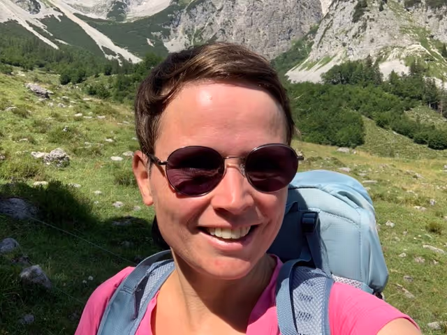 Person mit Sonnenbrille und Rucksack vor Berglandschaft